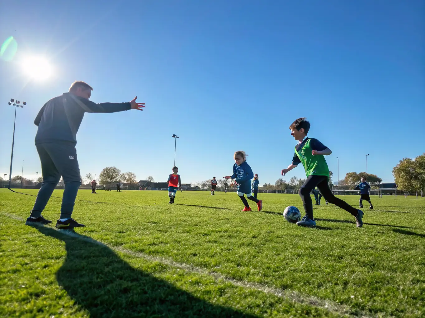 A group of children playing soccer in a park, wearing RED WOLF 23 jerseys, with coaches guiding them. The scene is vibrant and energetic, showcasing teamwork and fun.
